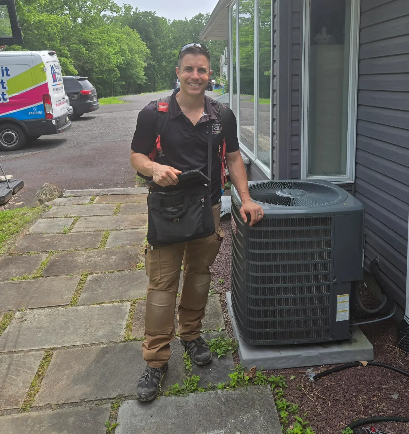 Plumb it Heat it Cool it technician beside a freshly serviced outdoor AC condenser