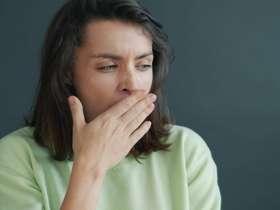 A tired woman covering a yawn with her hand.